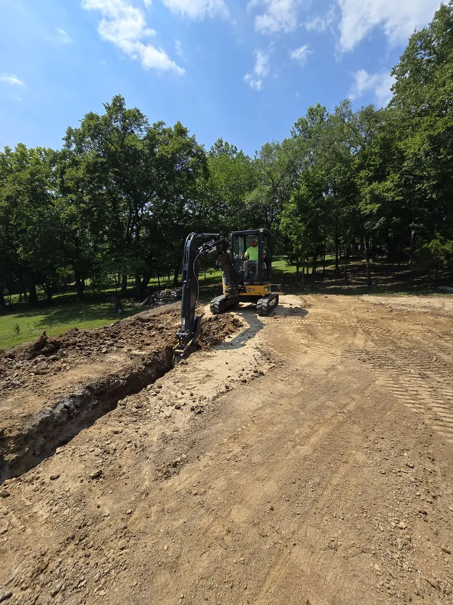 A compact excavator digging a trench on a sunny wooded lot
